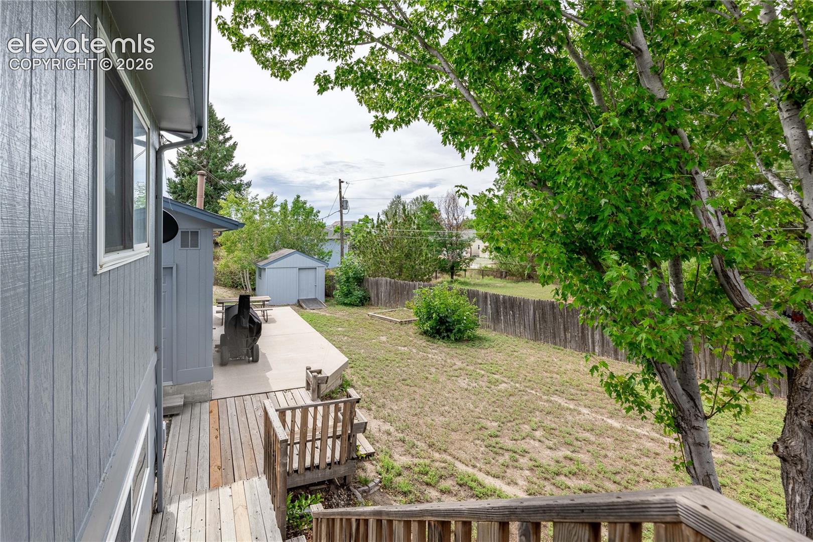 Rear yard featuring a wooden deck, concrete patio, detached storage shed, and perimeter wood fencing