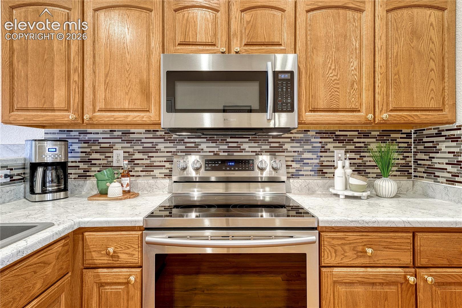 Up-close view of the stylish mosaic tile backsplash, built-in Samsung microwave, and glass-top range with 220V hookup
