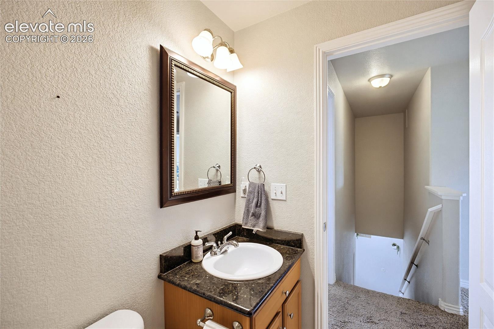 Vanity featuring a stone-finish countertop, undermount sink with a polished metal faucet, wood cabinetry, wall-mounted mirror, and decorative light fixture