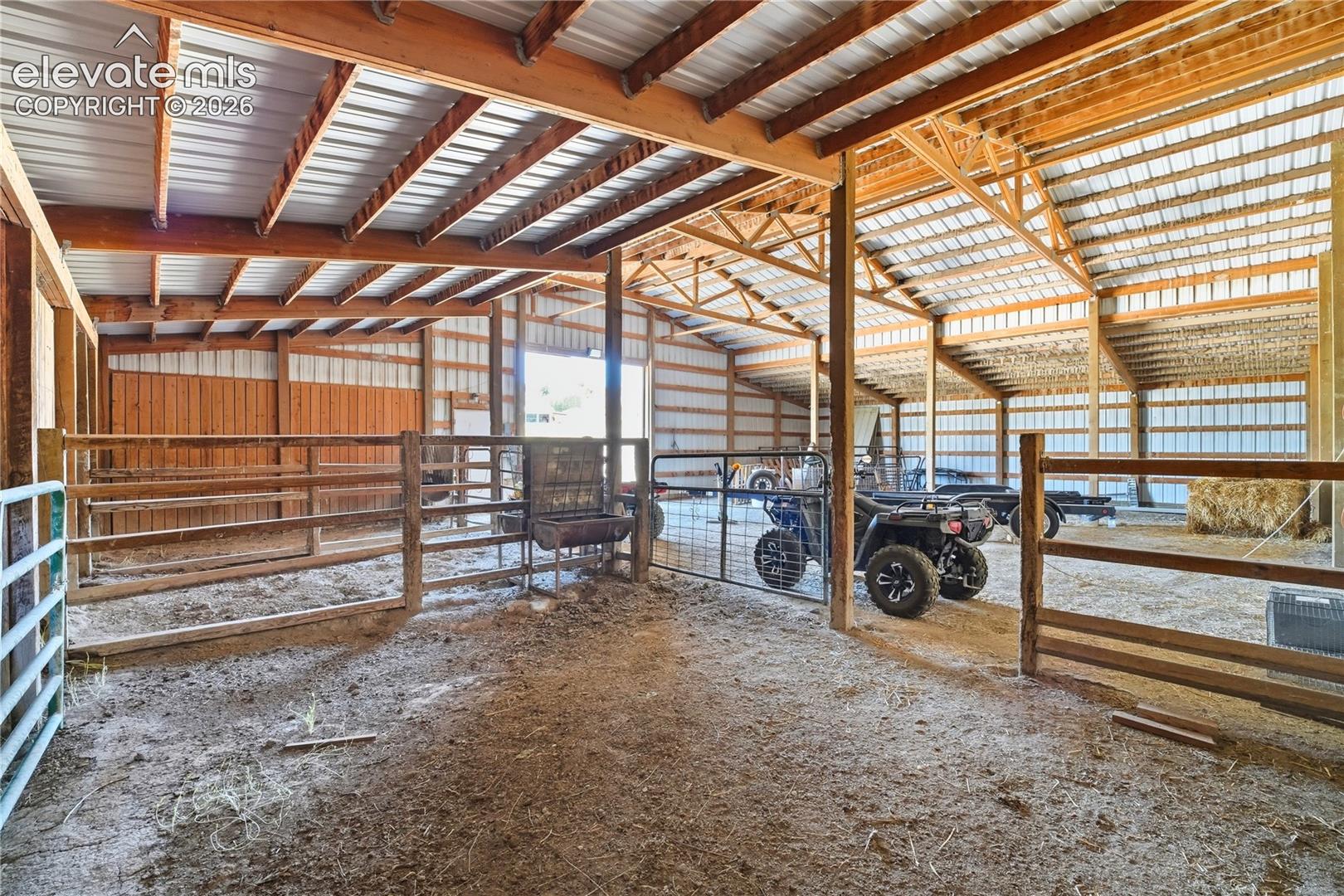 Barn structure with wooden framing, metal roofing, and multiple stalls with wooden fencing