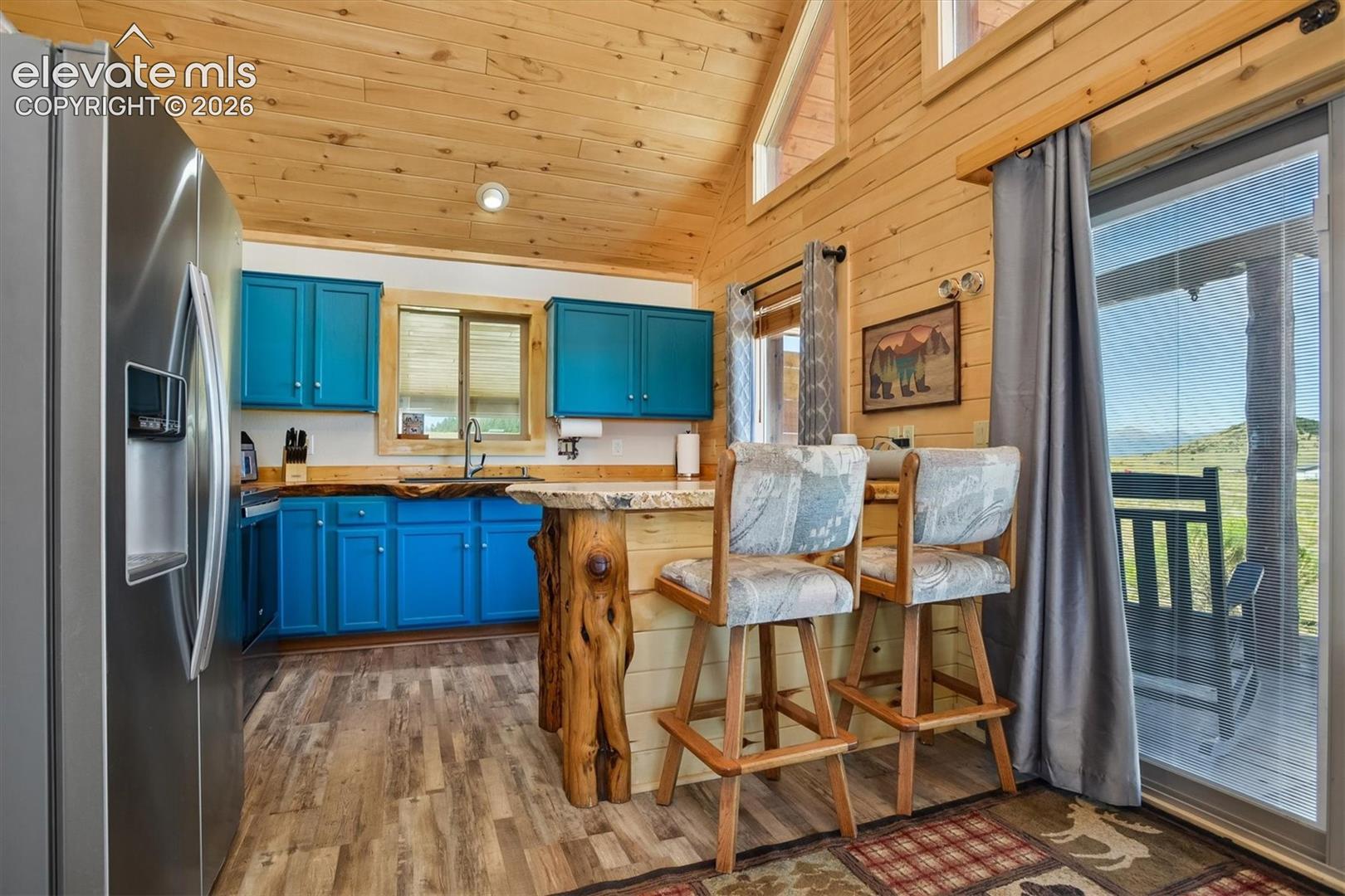 Kitchen featuring wood-finish flooring, vibrant blue cabinetry, stainless steel refrigerator, and a rustic wood breakfast bar with stone countertop