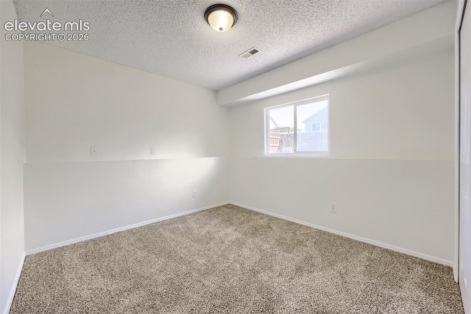 Recessed window with white trim, neutral carpeting, flush-mount ceiling light fixture, and textured ceiling