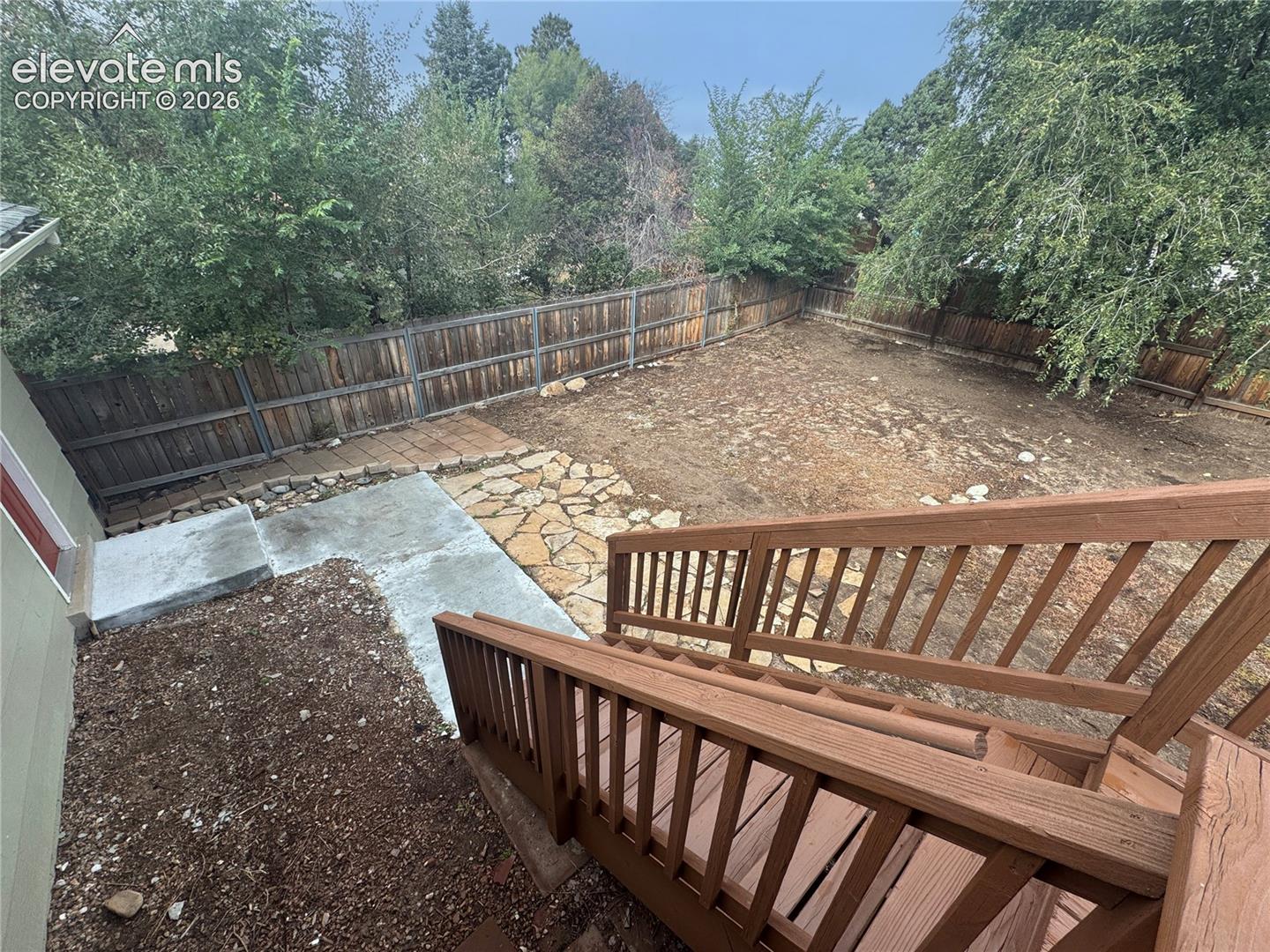 Rear exterior space featuring a wood-railed staircase, concrete patio, stone hardscaping, and perimeter wood privacy fencing