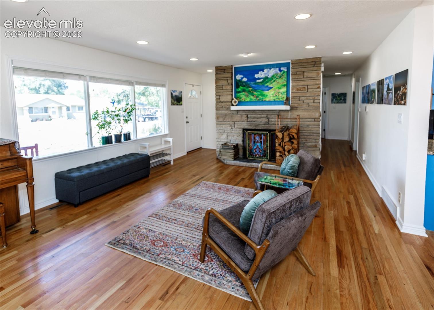 Hardwood flooring throughout, stone fireplace with hearth, recessed lighting, and large windows