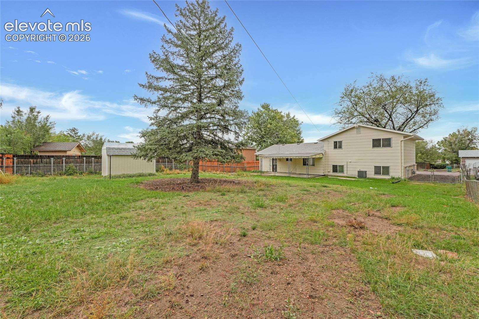 Expansive grassy yard with mature trees, detached storage shed, and fenced perimeter