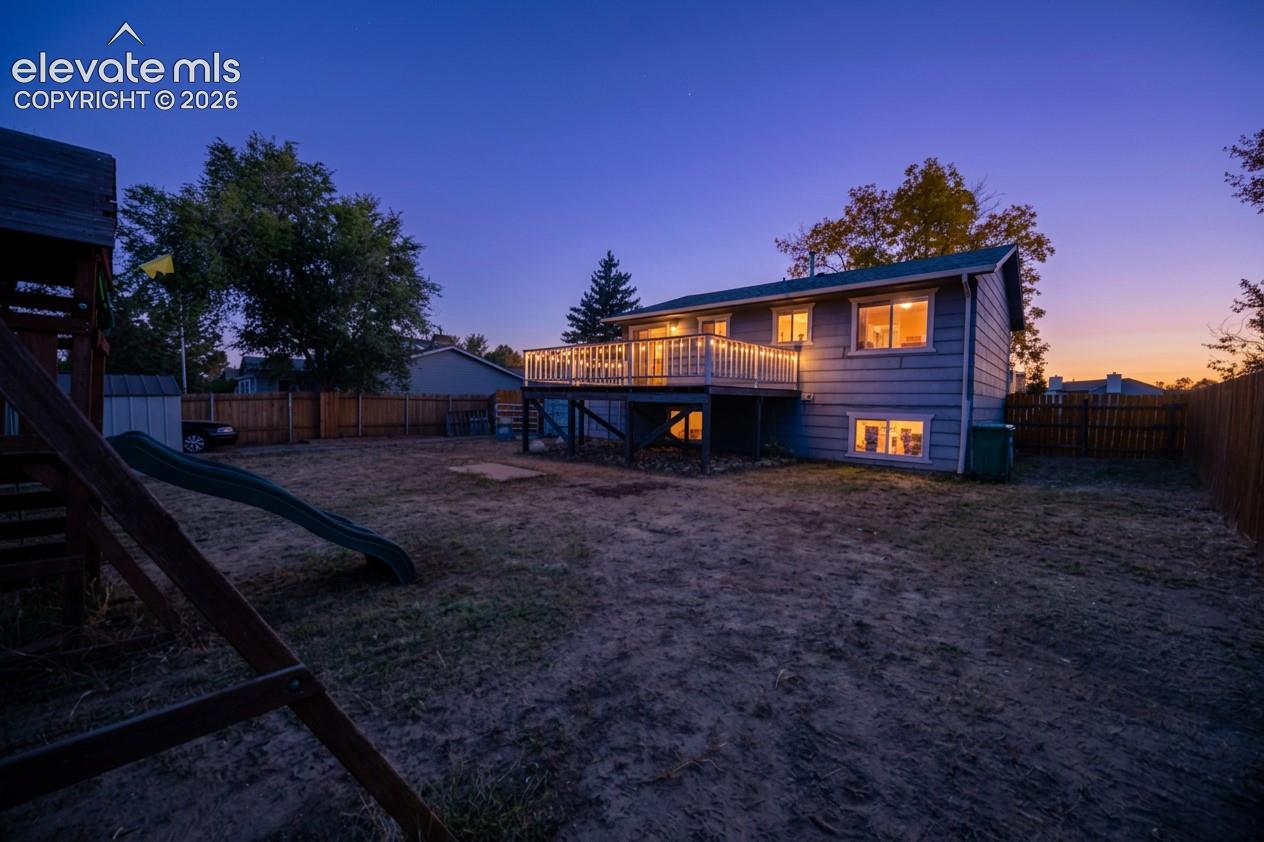 Two-story residence with a raised deck, light-colored siding, and a fenced backyard