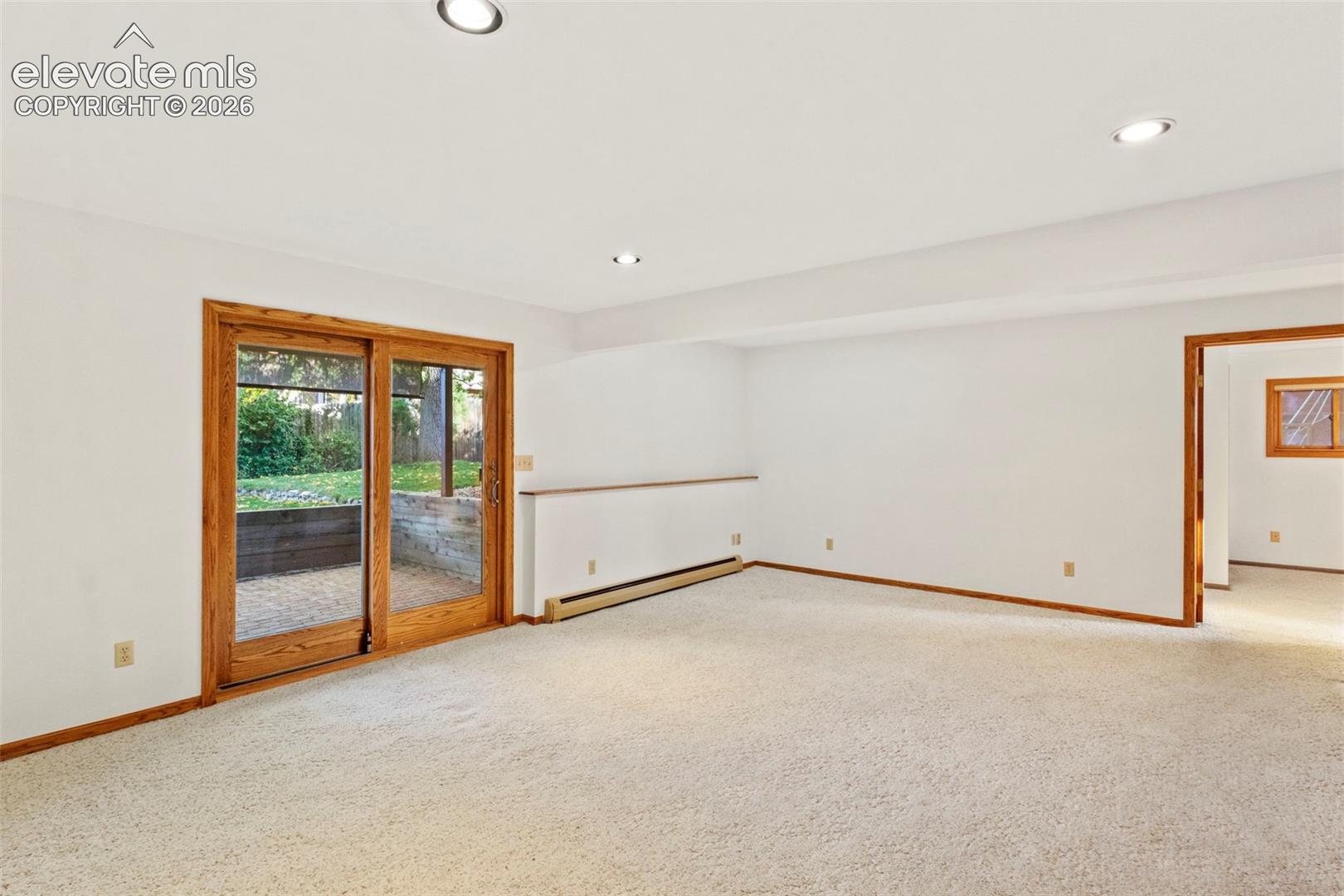 Neutral-toned carpeted interior featuring recessed lighting, natural wood-frame sliding glass doors, and a wood-cased entryway