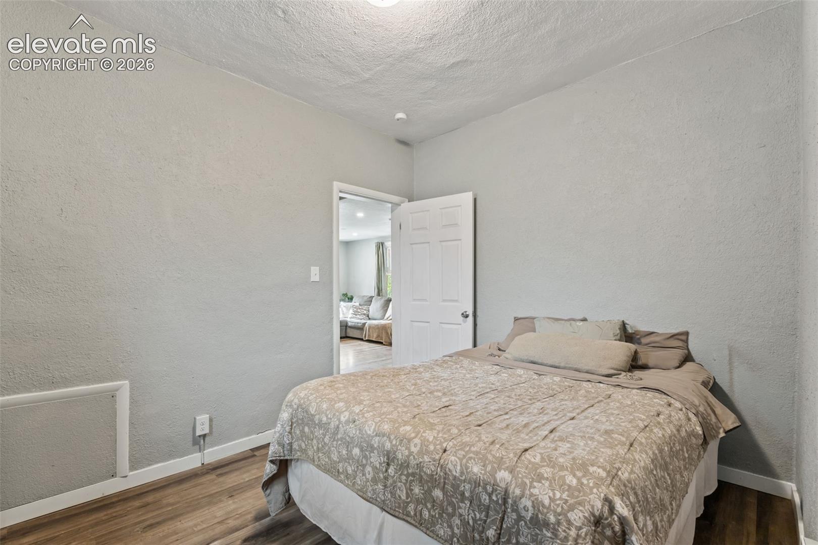 Bedroom featuring wood-finish flooring, light gray textured walls, and a white interior door