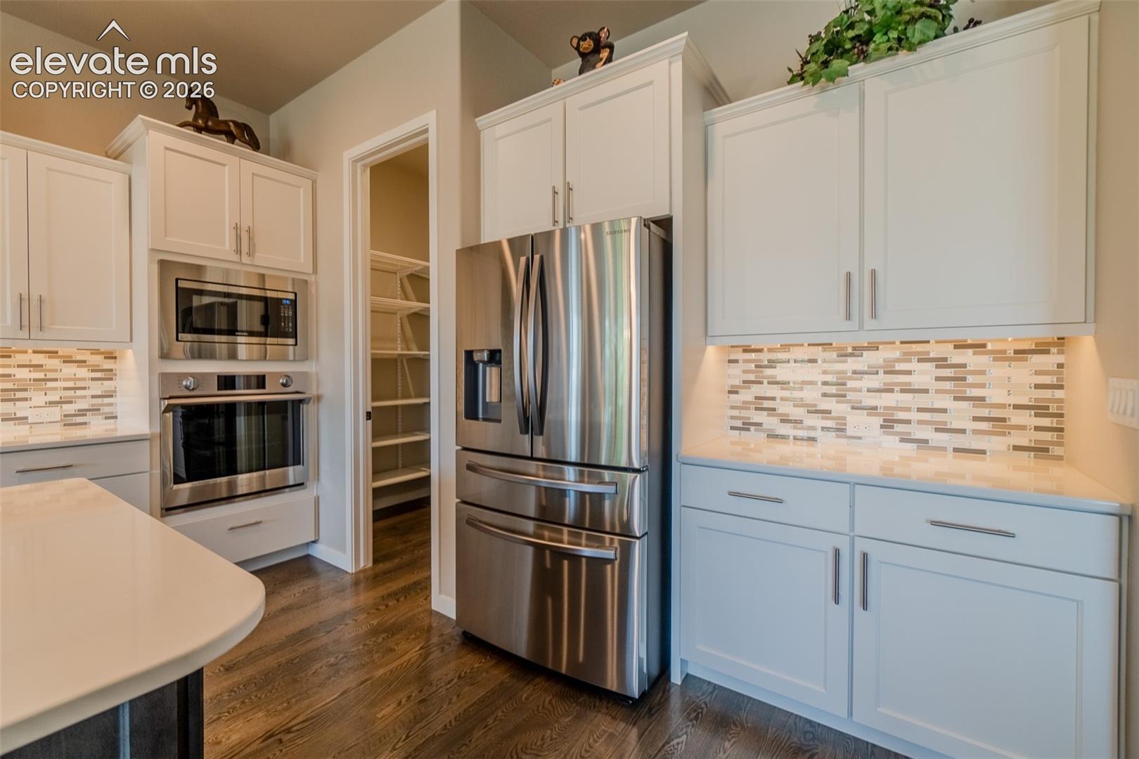 Modern kitchen featuring white shaker cabinetry, stainless steel appliances, and wood-finish flooring