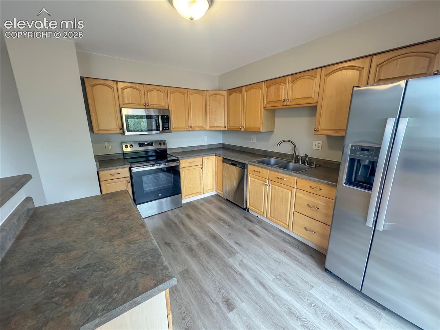 Kitchen featuring wood-finish cabinetry, stainless steel appliances, dual-basin sink, and wood-finish flooring