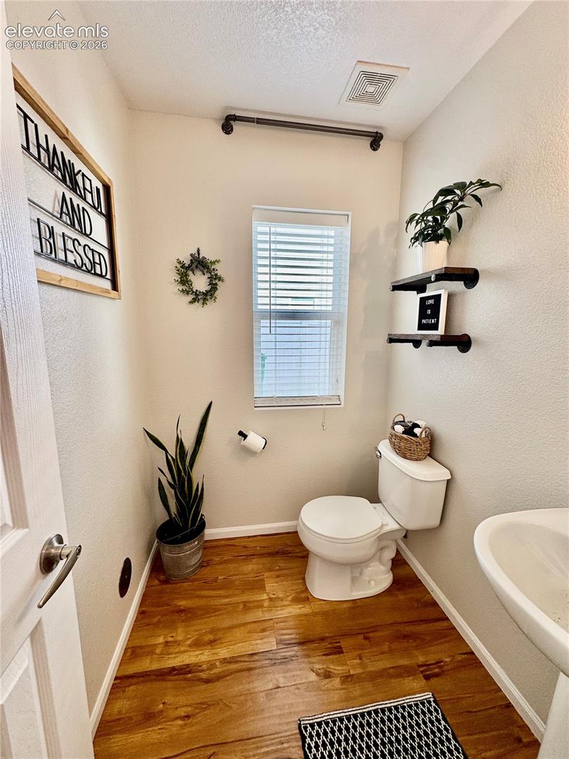 Powder room featuring wood-finish flooring, a contemporary toilet, and a pedestal sink