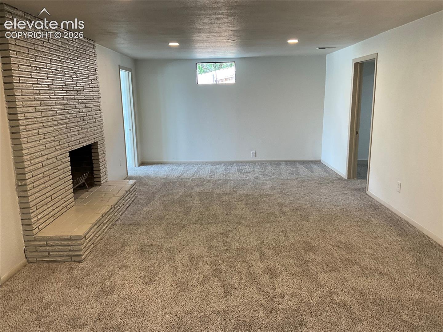 Expansive room featuring a brick fireplace with a raised hearth, light-toned carpet flooring, white walls, and recessed lighting