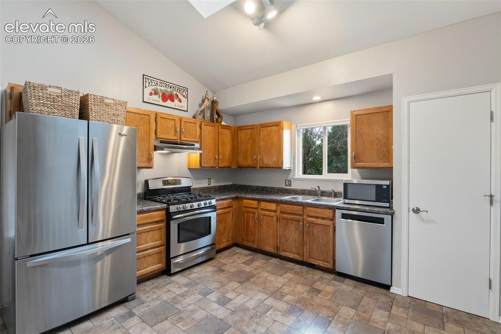 Kitchen featuring wood cabinetry, stainless steel appliances, a double basin sink, and a window