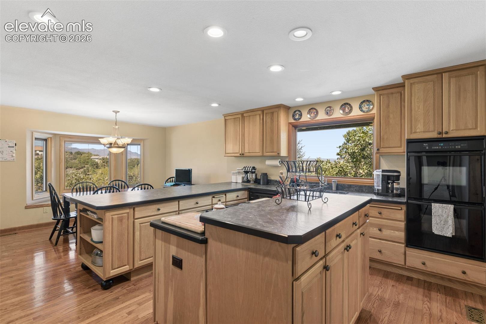 Kitchen featuring wood cabinetry, solid-surface countertops, center island, integrated double wall oven, and wood-finish flooring