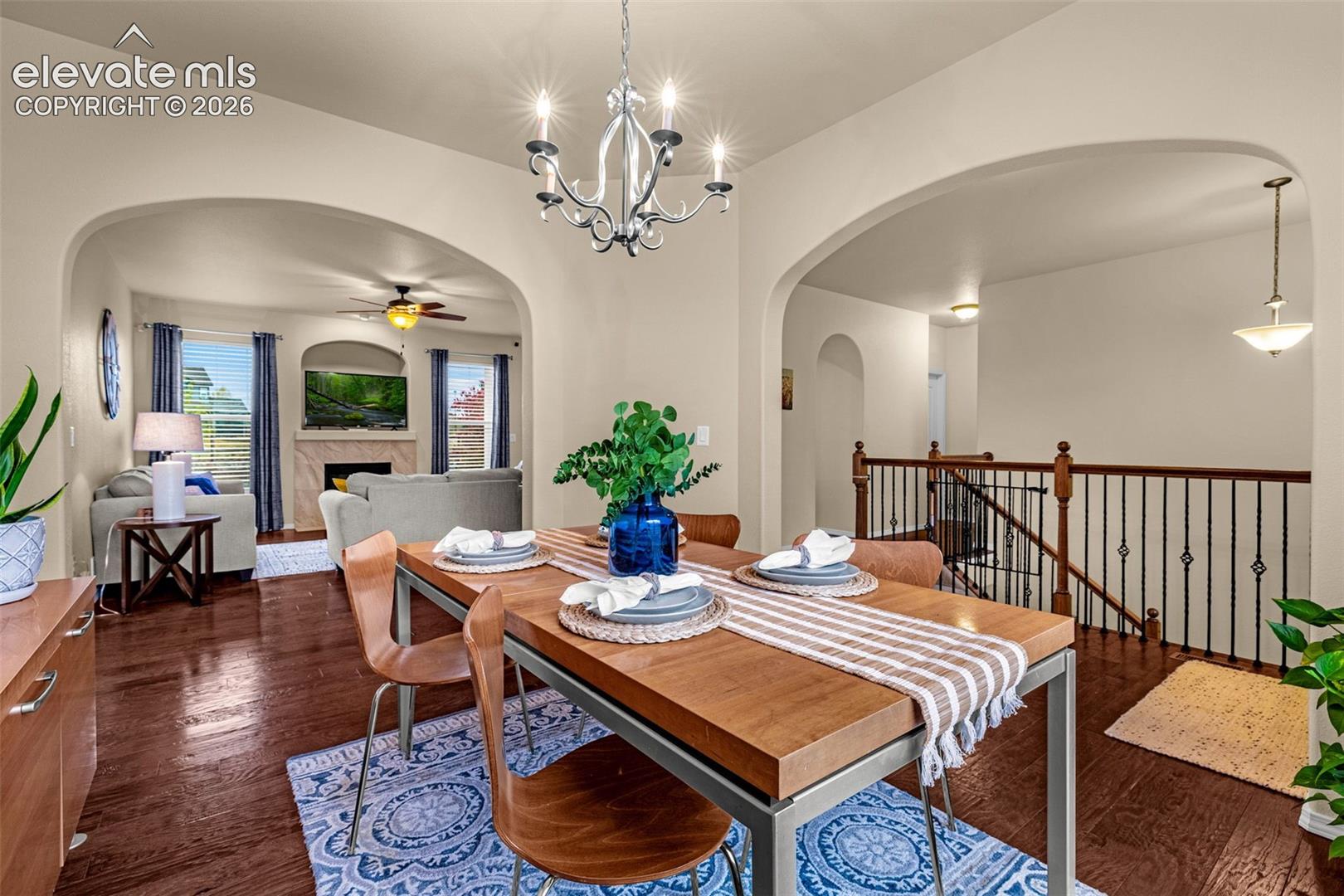 Open-concept interior featuring arched entryways, wood-finish flooring, a multi-arm metallic chandelier, and a metal-spindle staircase railing