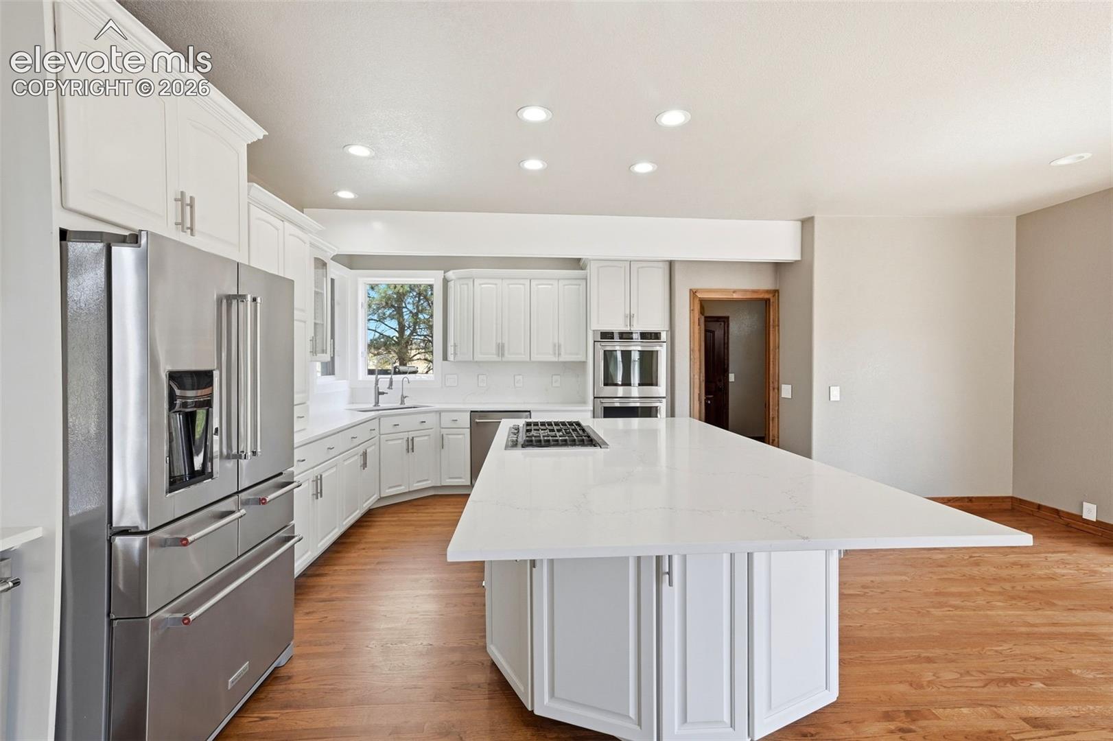 Modern kitchen featuring a large central island with a cooktop, white cabinetry, integrated stainless steel appliances, and wood-finish flooring