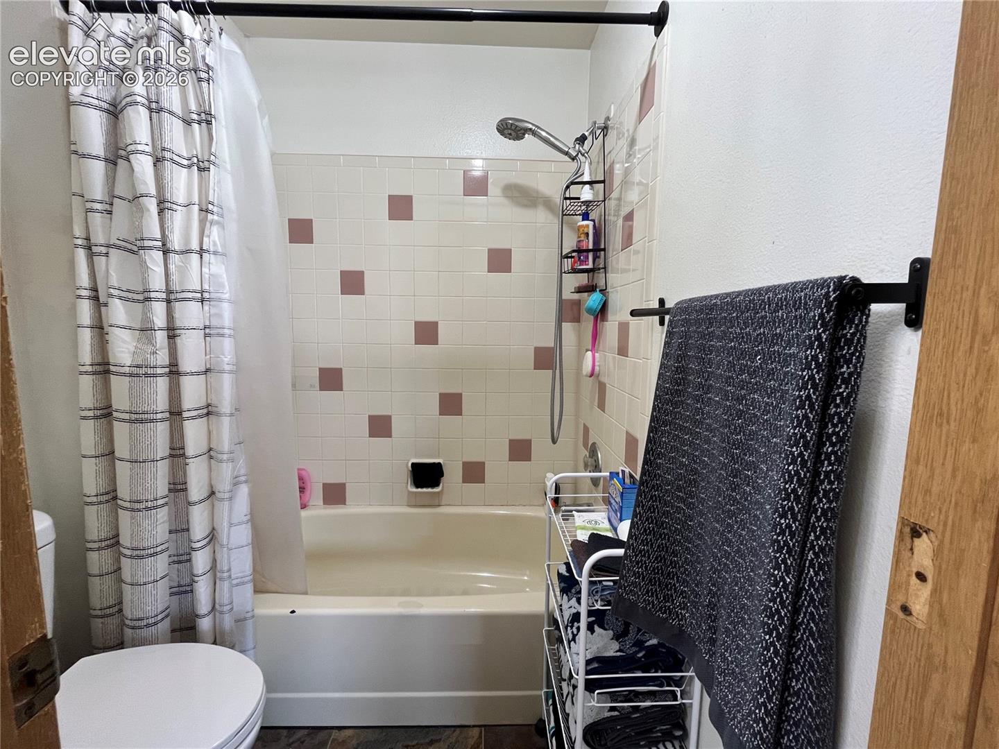 Bathtub with integrated shower head and ceramic tile surround featuring a subtle accent pattern