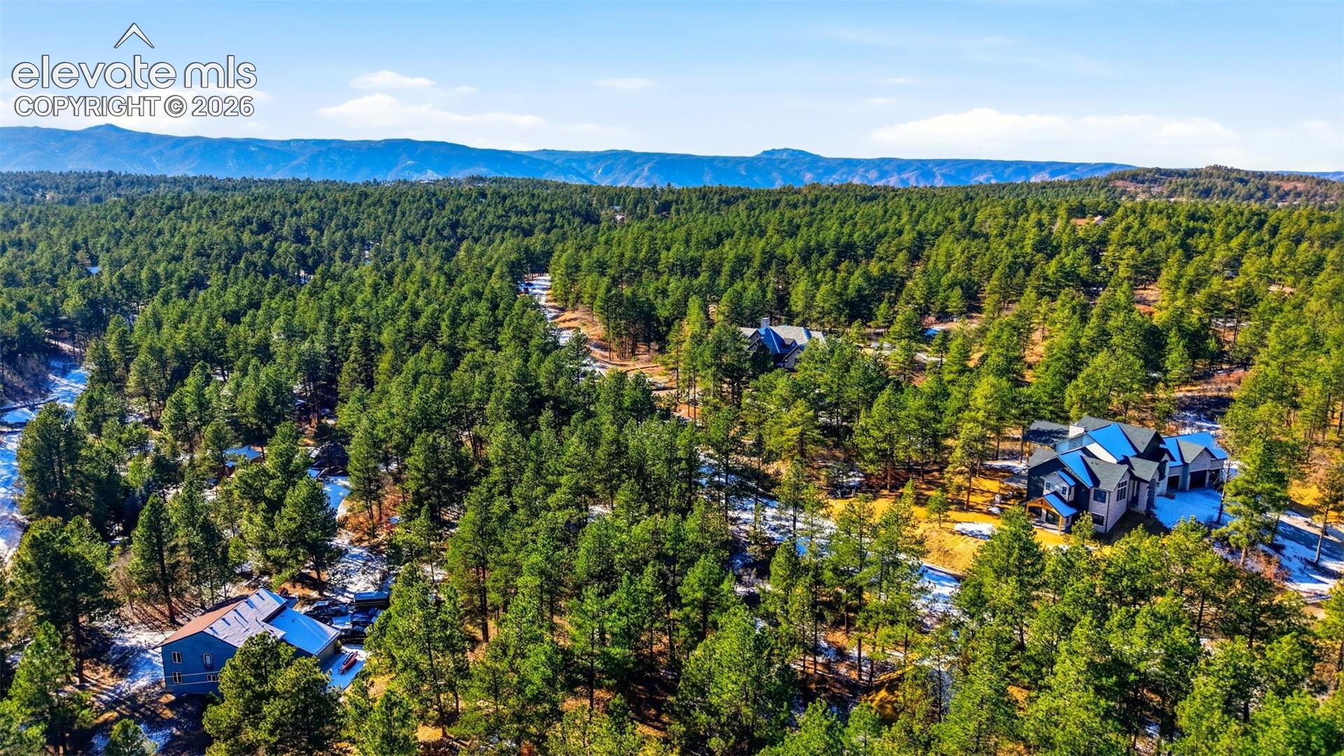 Expansive treed landscape with multiple residential structures, featuring surrounding mountains and clear skies