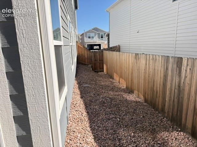 Gravel pathway alongside a home with horizontal siding and multiple windows, bordered by a wood fence with a gate