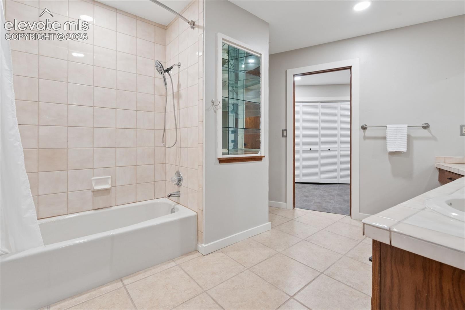 Tile flooring, built-in bathtub with tile surround, recessed lighting, and a built-in display cabinet