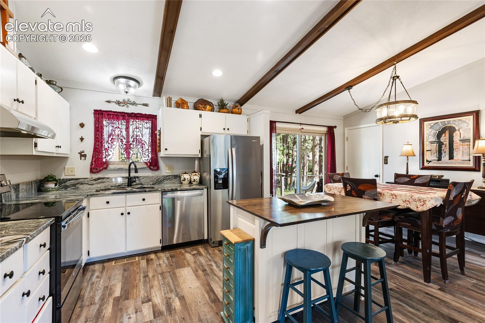Kitchen featuring wood-finish flooring, white cabinetry, stainless steel appliances, and a central island with bar seating