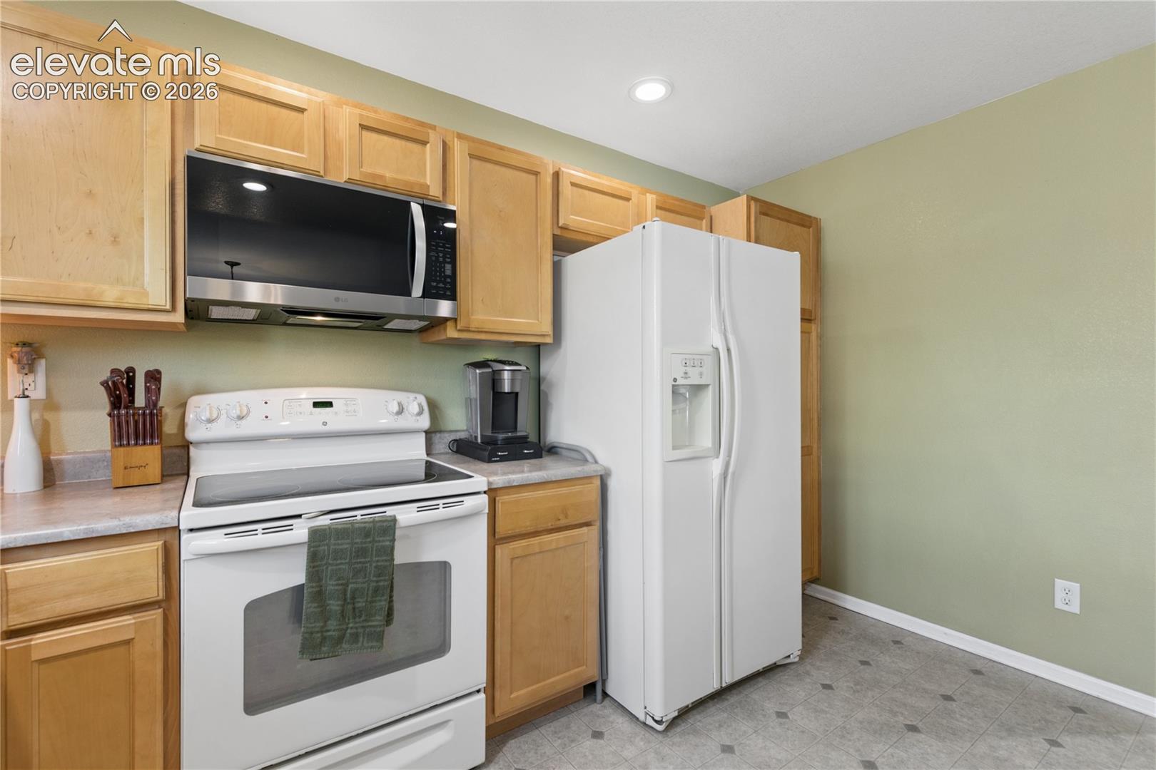 Kitchen featuring wood-finish cabinetry, built-in microwave, white electric range, and white side-by-side refrigerator with ice and water dispenser