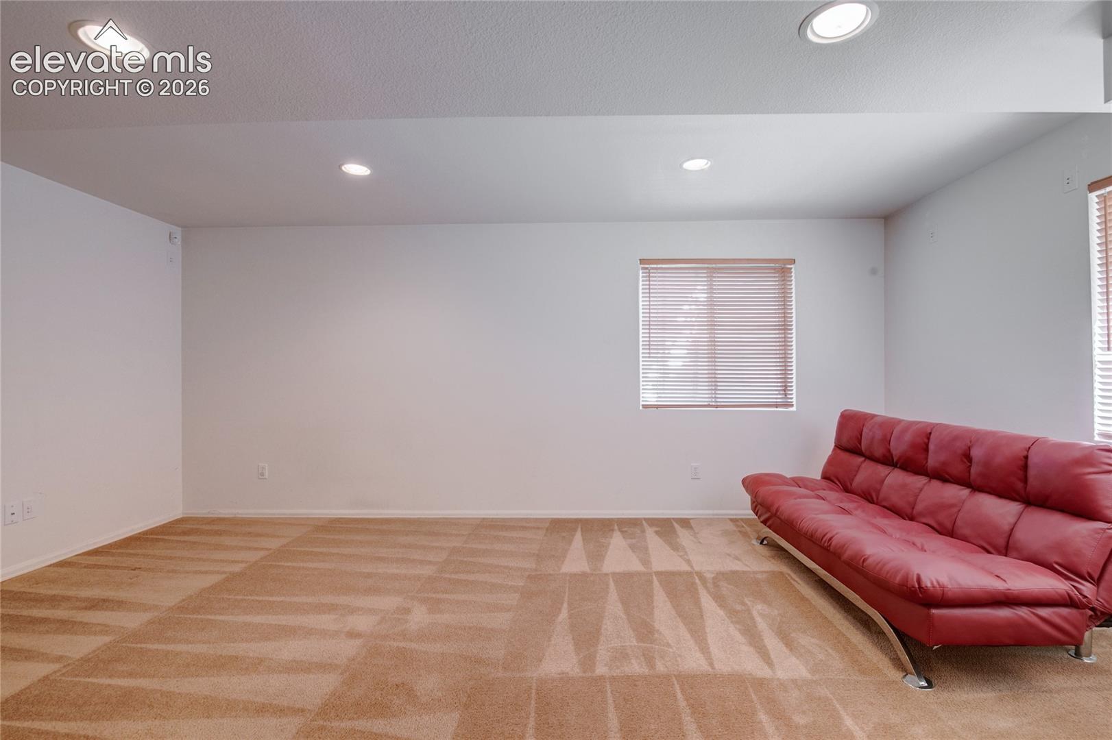 Spacious room featuring neutral carpeting with a patterned design, recessed lighting, and multiple windows with blinds