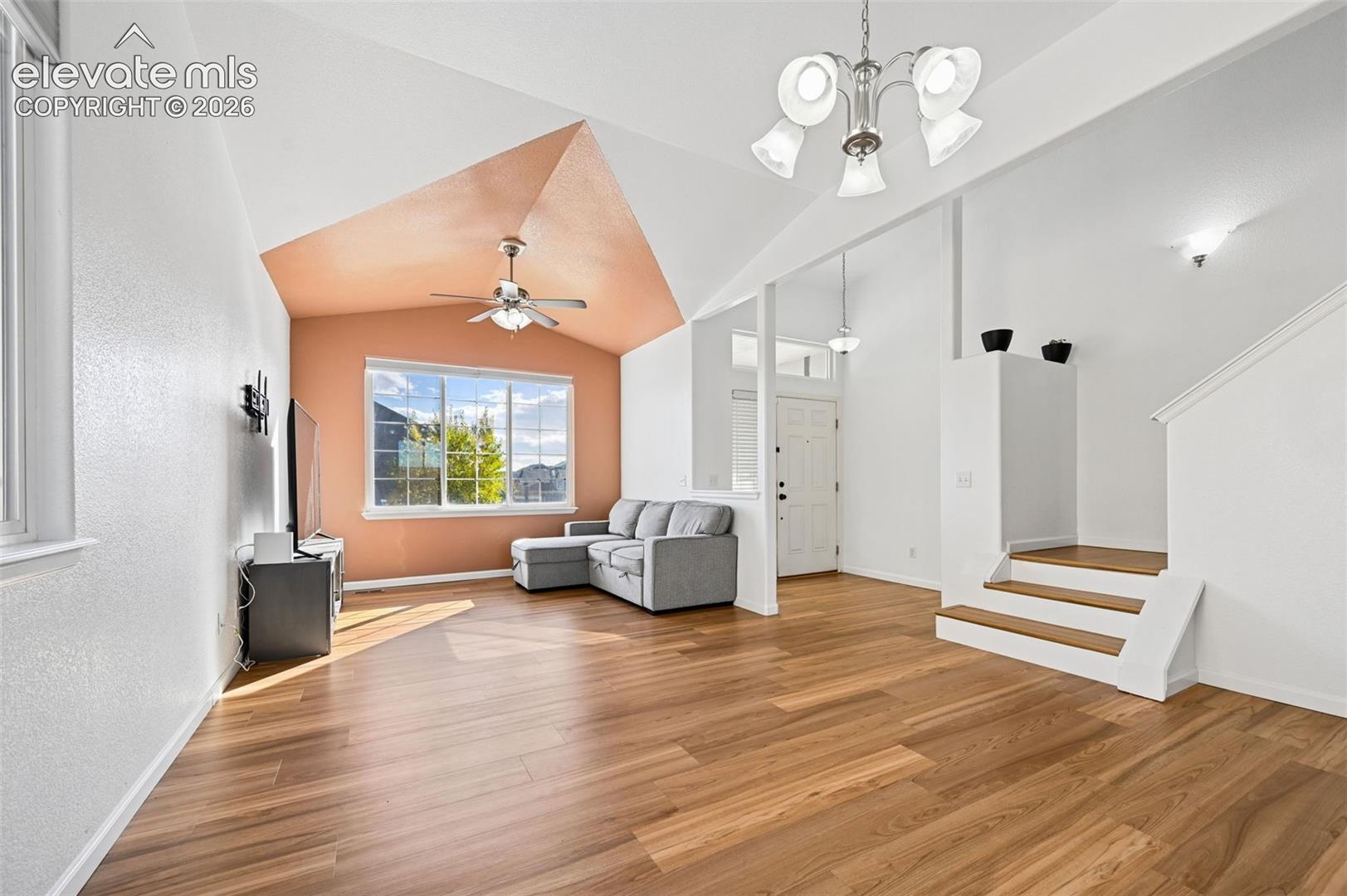 Vaulted ceilings featuring a multi-tone accent wall, wood-finish flooring, a multi-arm brushed nickel chandelier, and a recessed window
