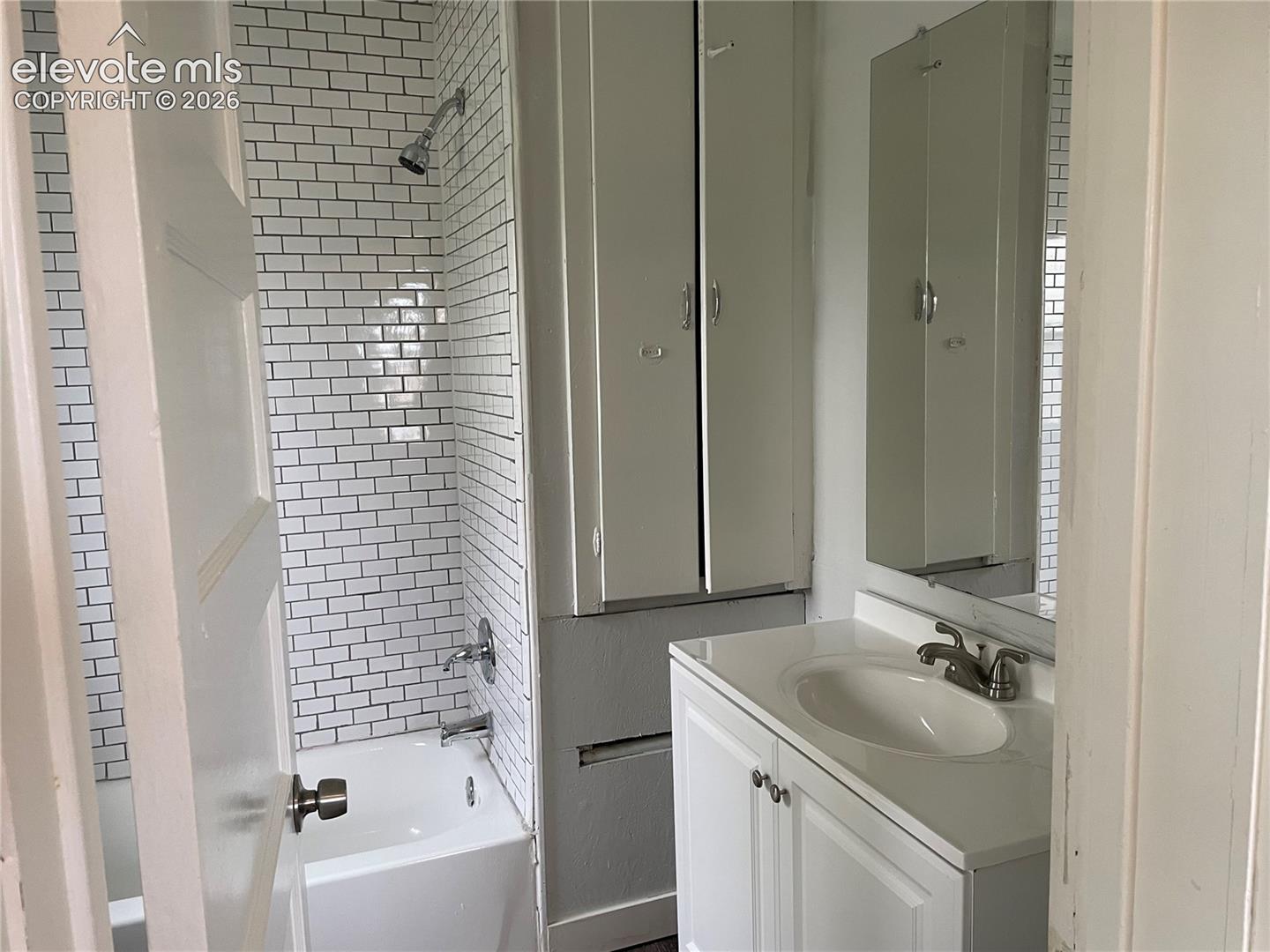 Bathroom featuring a white subway tile shower surround, a built-in tub with chrome fixtures, a vanity with an integrated sink, and an overhead mirror