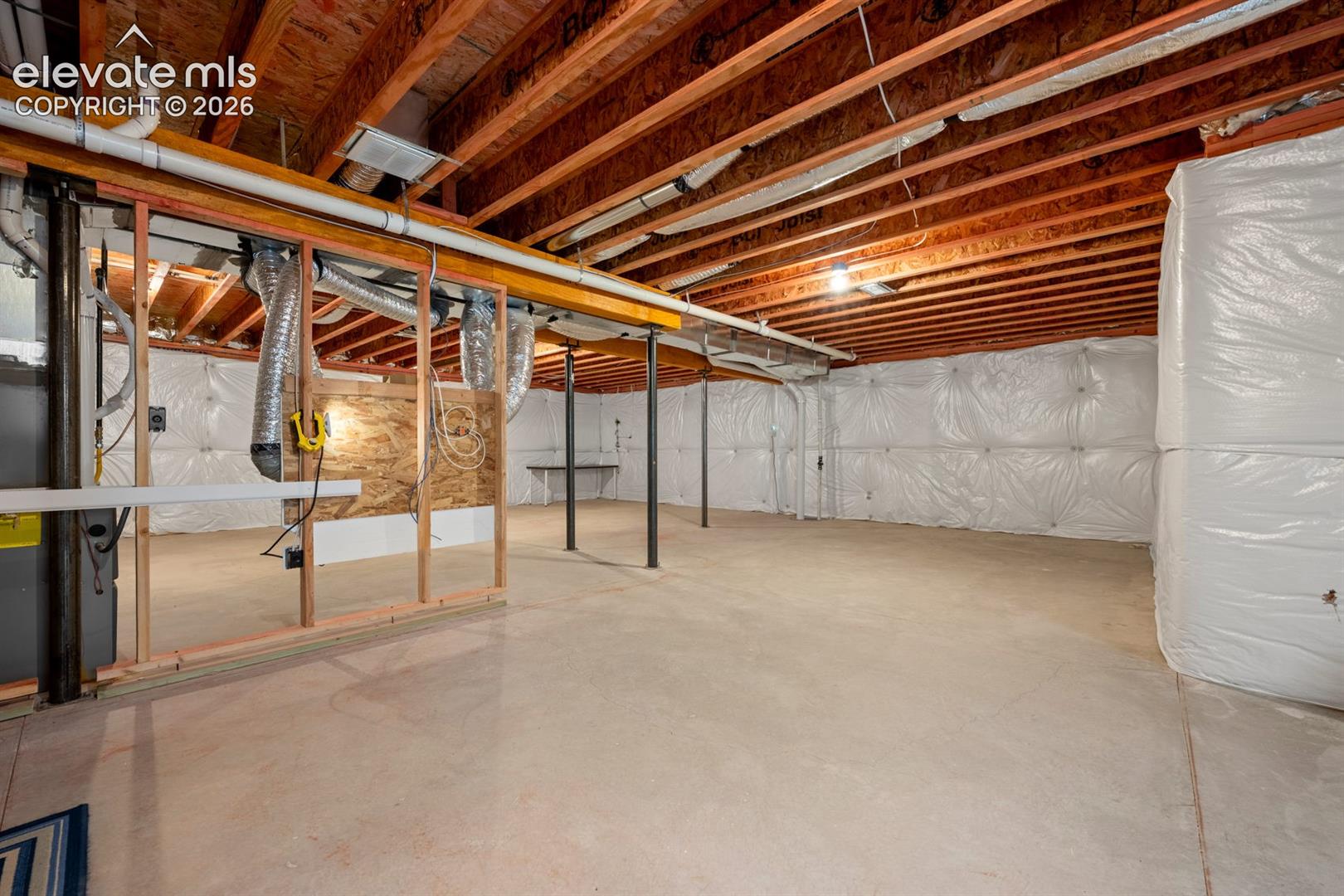 Unfinished lower level featuring exposed wood joists, concrete flooring, plastic vapor-barrier wall insulation, and support columns