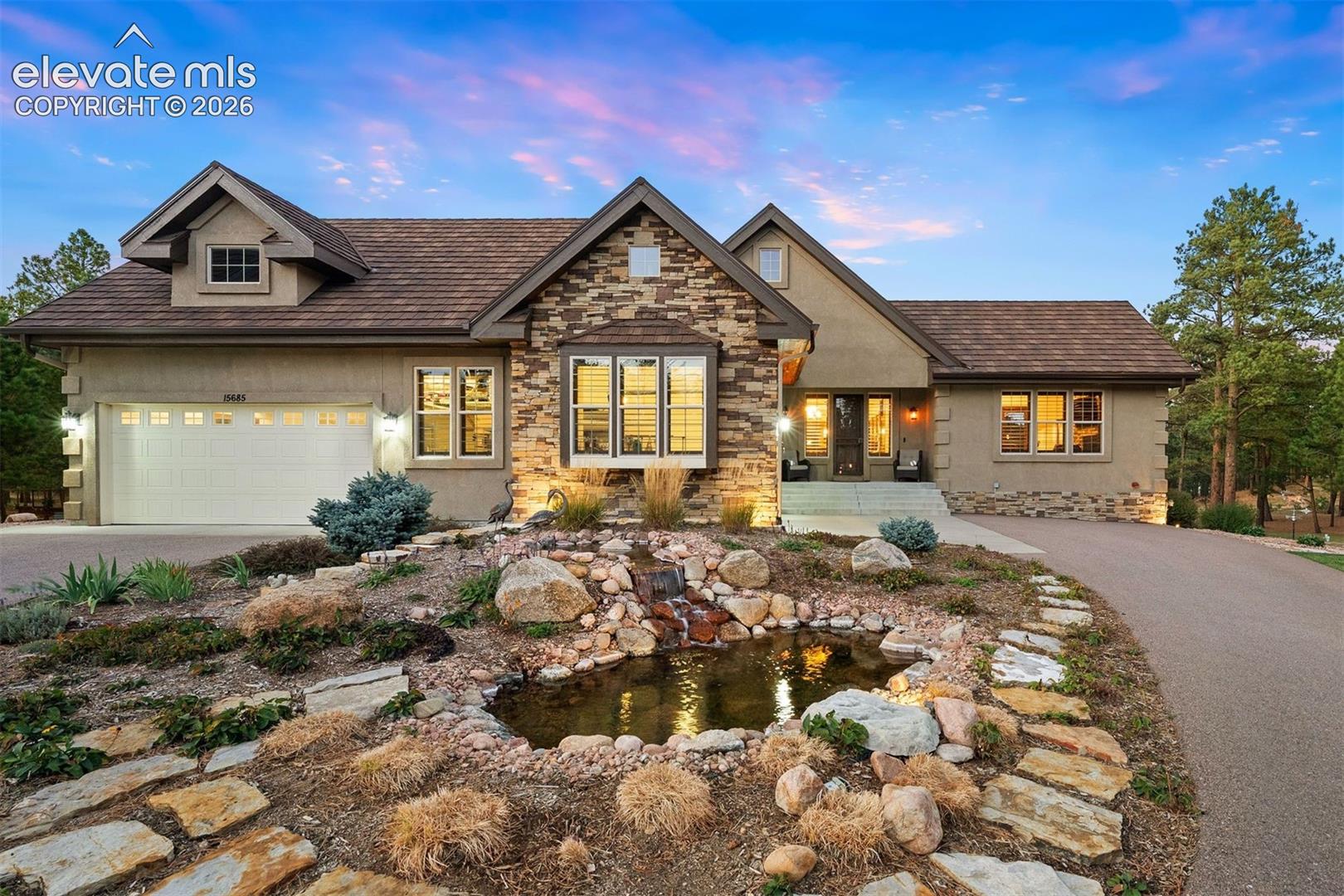 Exterior featuring a stone-veneer facade, multi-gabled roofline, three-car garage, and a landscaped front yard with a stone-lined pond and water feature