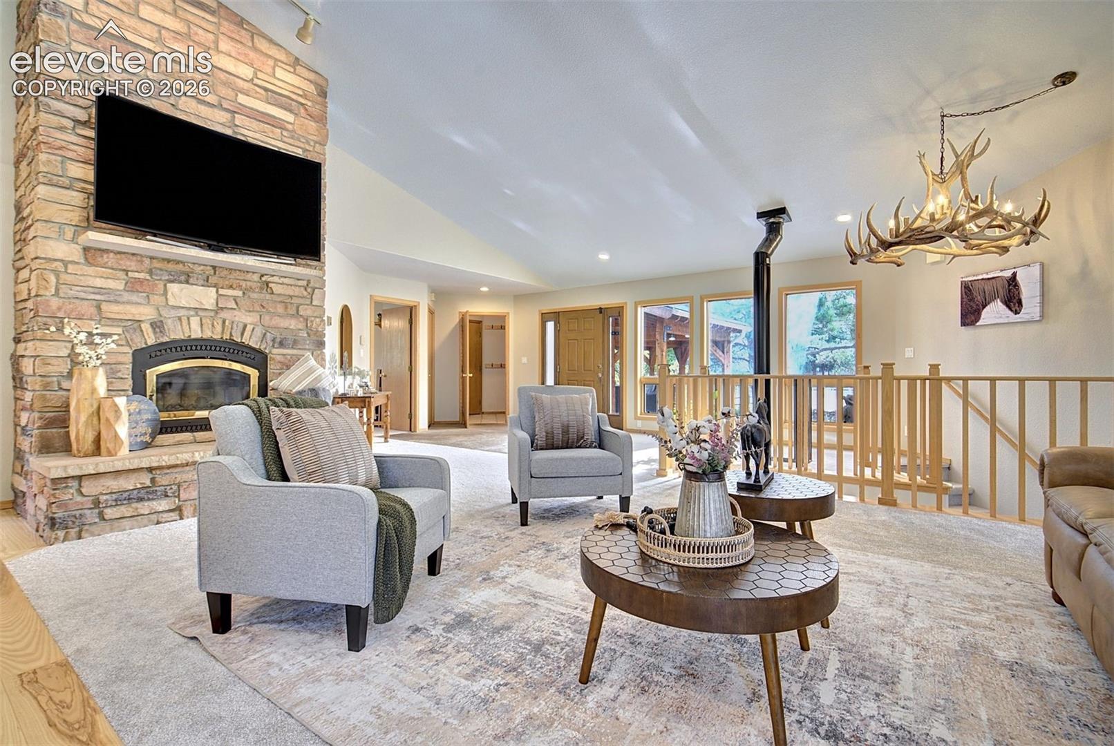 Floor-to-ceiling stone fireplace with an integrated hearth, vaulted ceilings, and a suspended antler chandelier