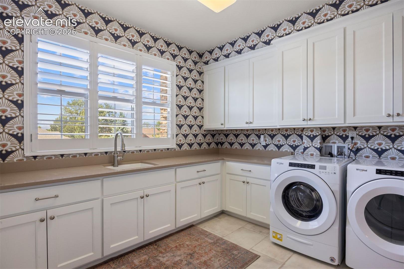 Utility room featuring extensive white cabinetry, a built-in sink with a gooseneck faucet, light-colored countertops, and patterned wallpaper