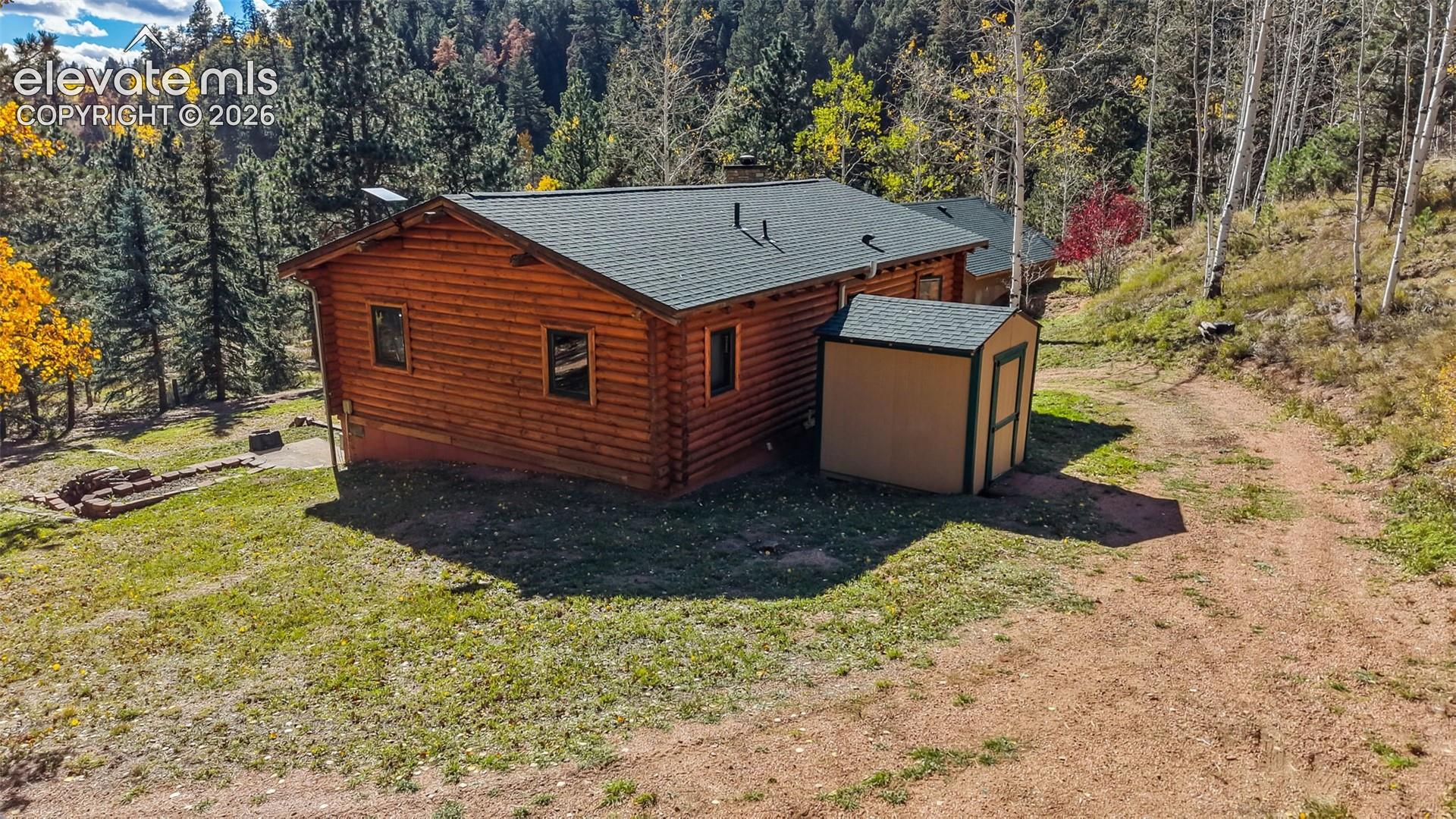 Log exterior cabin featuring a shingle roof, integrated storage shed, and surrounding forest landscape