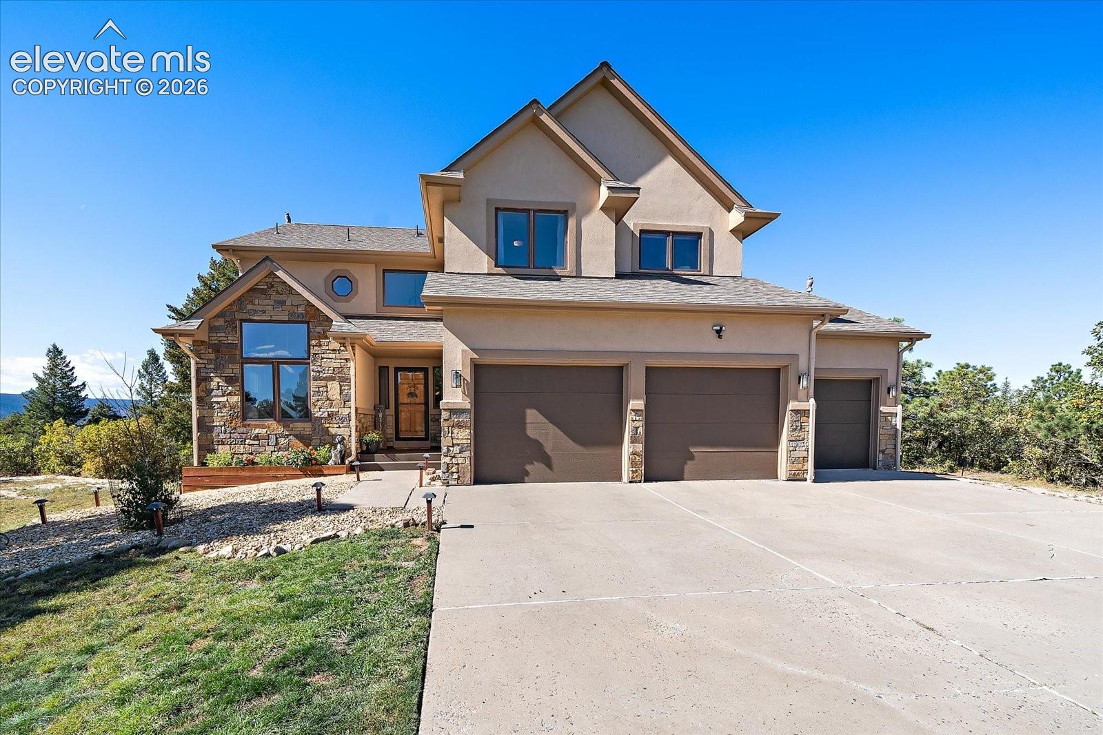 Stucco and stone exterior facade featuring a multi-gabled roofline, three-car garage, and concrete driveway