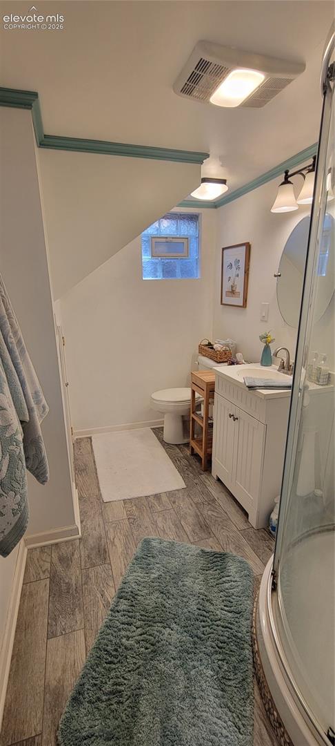 Downstairs bathroom featuring a glass-enclosed corner shower, white vanity with integrated sink, oval wall mirror, modern two-light fixture, and wood-finish flooring