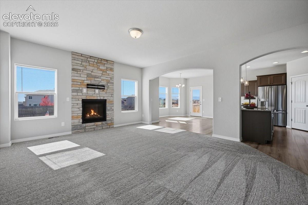 Living area featuring a floor-to-ceiling stone fireplace, arched architectural detailing, and wood-finish flooring in the kitchen