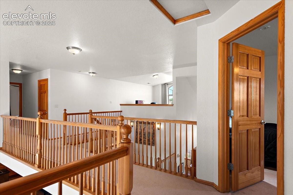 Upper-level landing featuring wood balusters and railings, a paneled wood door, recessed ceiling lighting, and light-colored carpeting