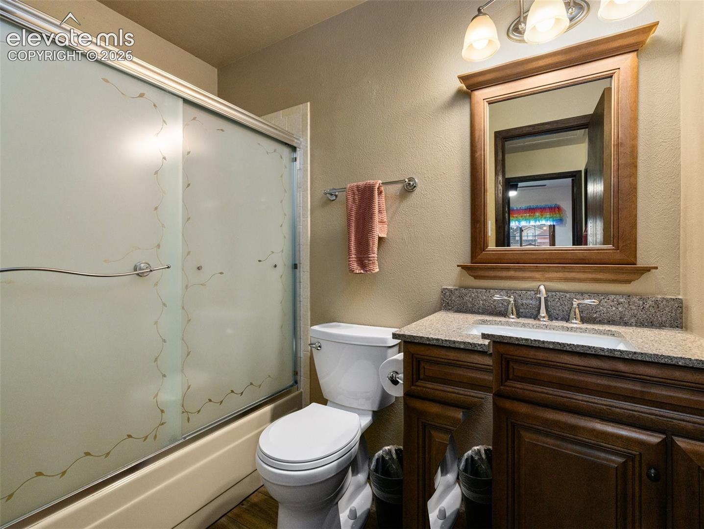 Bathroom featuring a wood-finish vanity with a stone countertop, an undermount sink, and a framed mirror