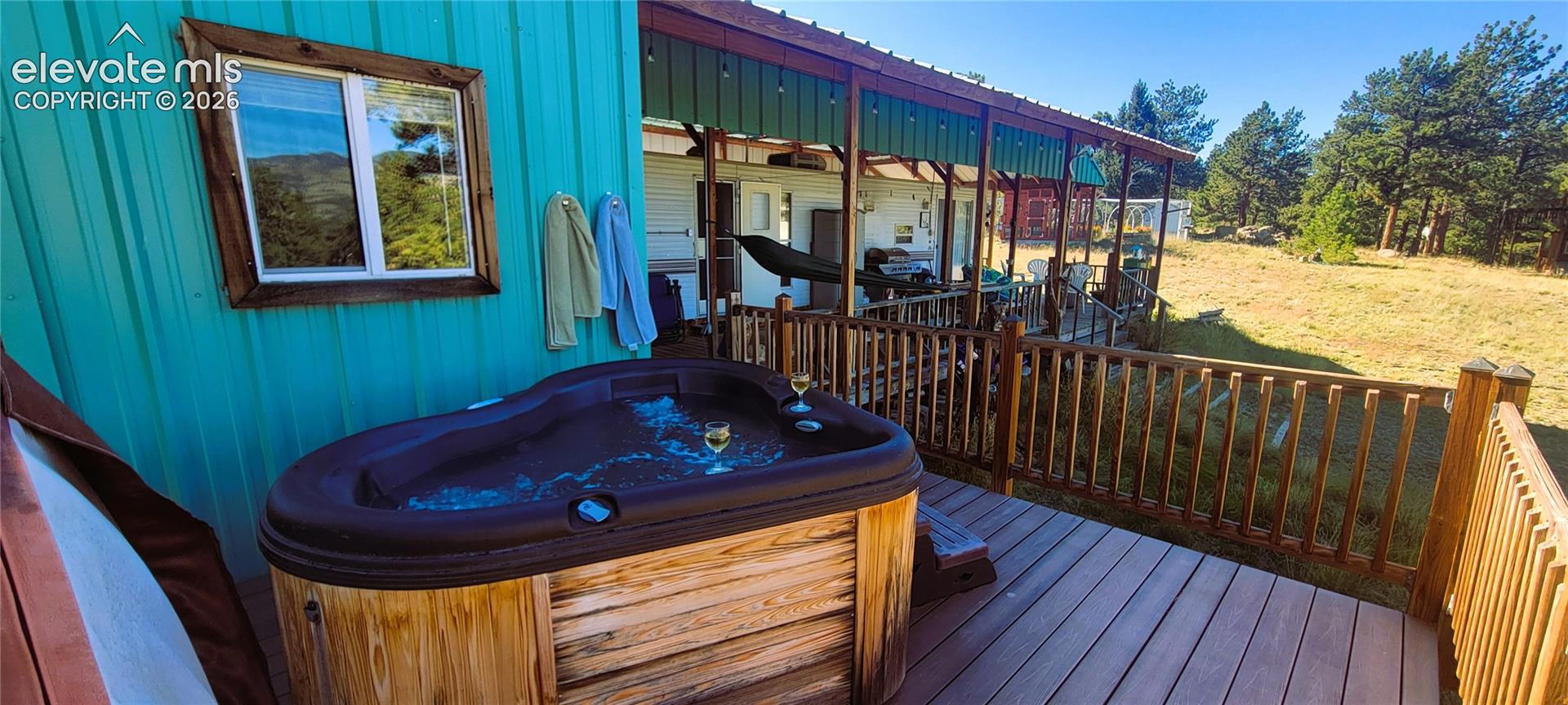 Expansive wood-finish deck with a built-in hot tub, wood-finish railing, and covered patio