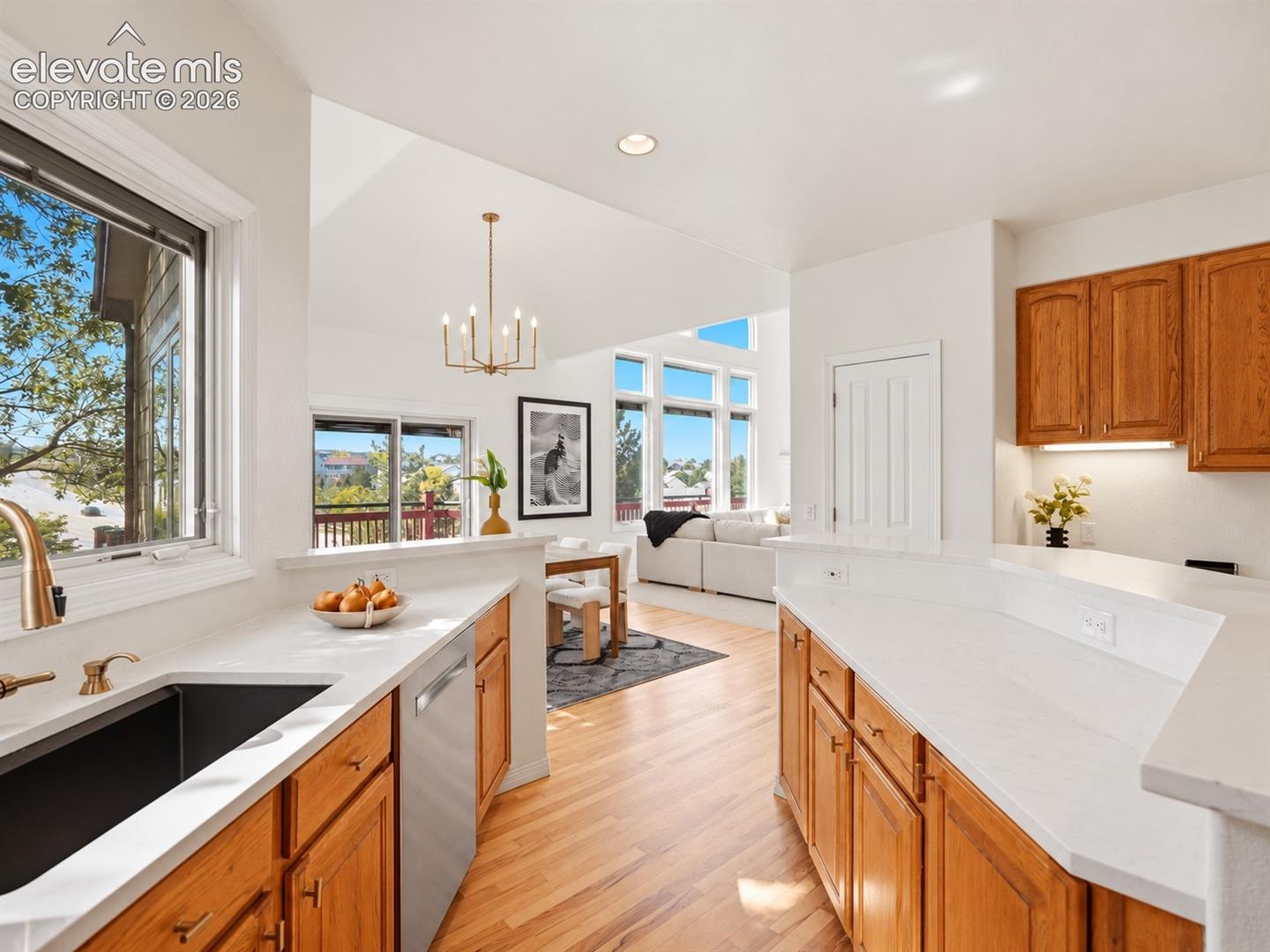 Kitchen featuring wood cabinetry, white countertops, a deep-basin sink with a gold-tone faucet, wood-finish flooring, and a vaulted ceiling with a chandelier