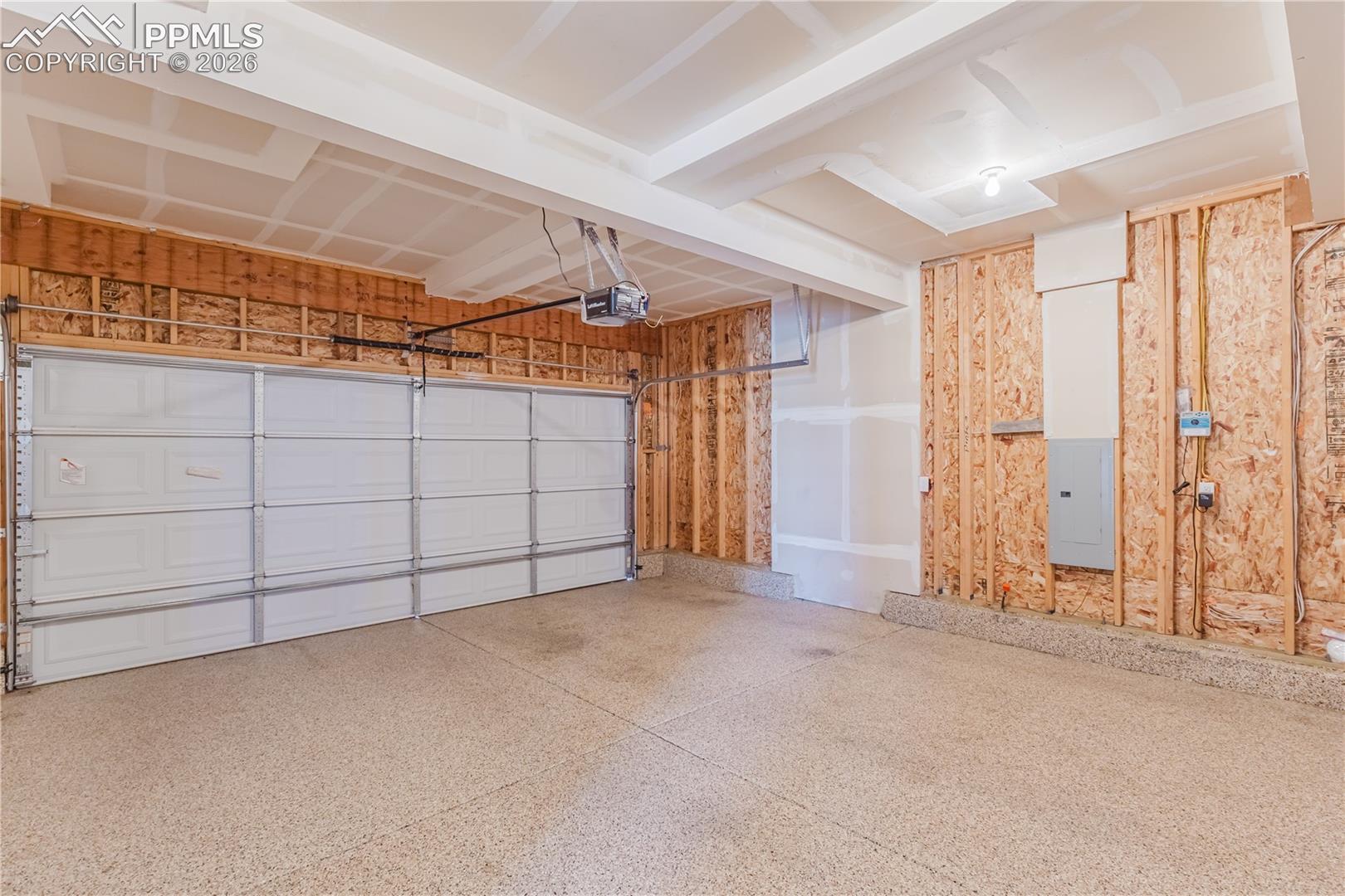 Garage featuring epoxied floor, electric panel and a garage door opener