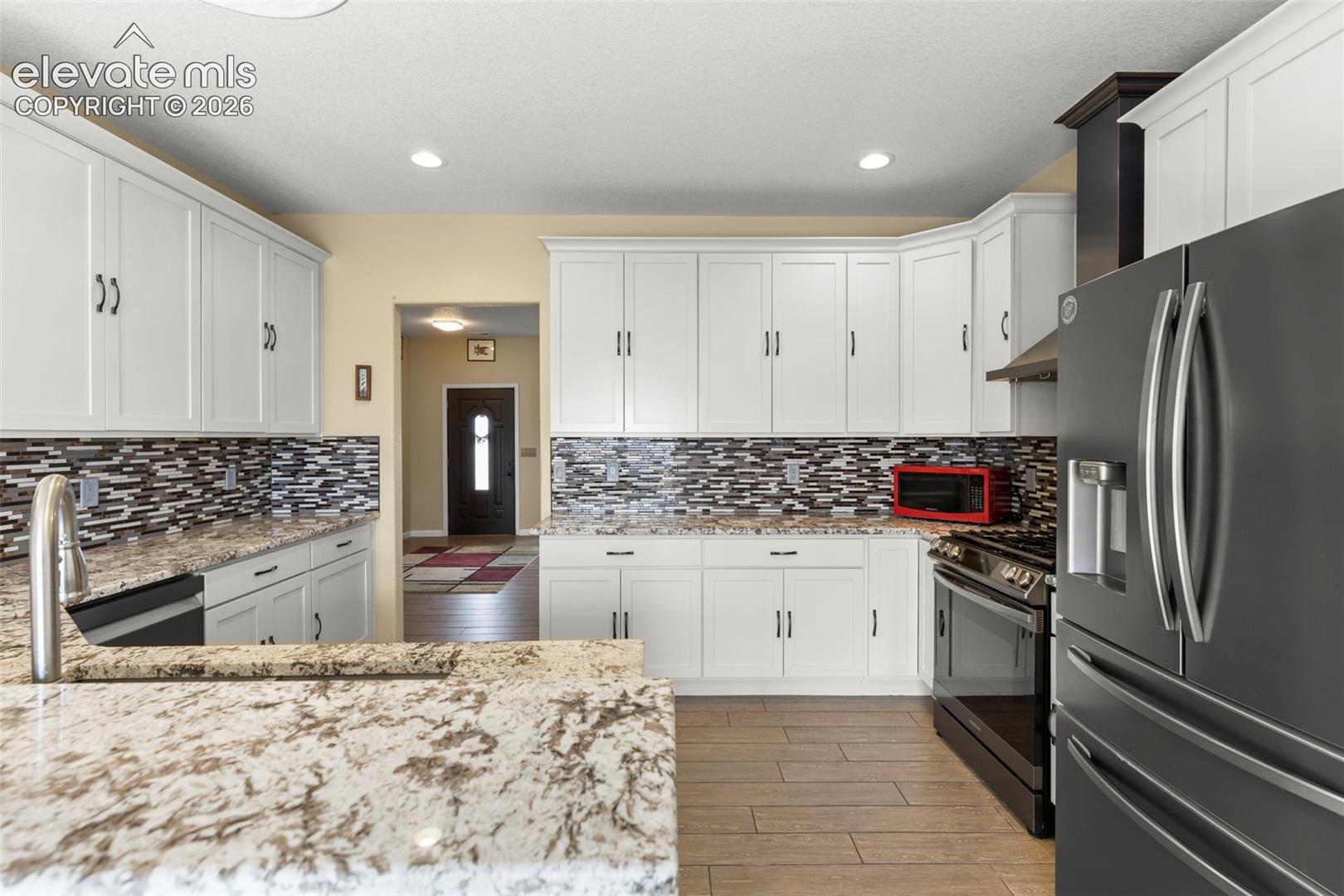 Kitchen featuring white cabinetry, stone-finish countertops, decorative multi-toned tile backsplash, recessed lighting, and wood-finish flooring