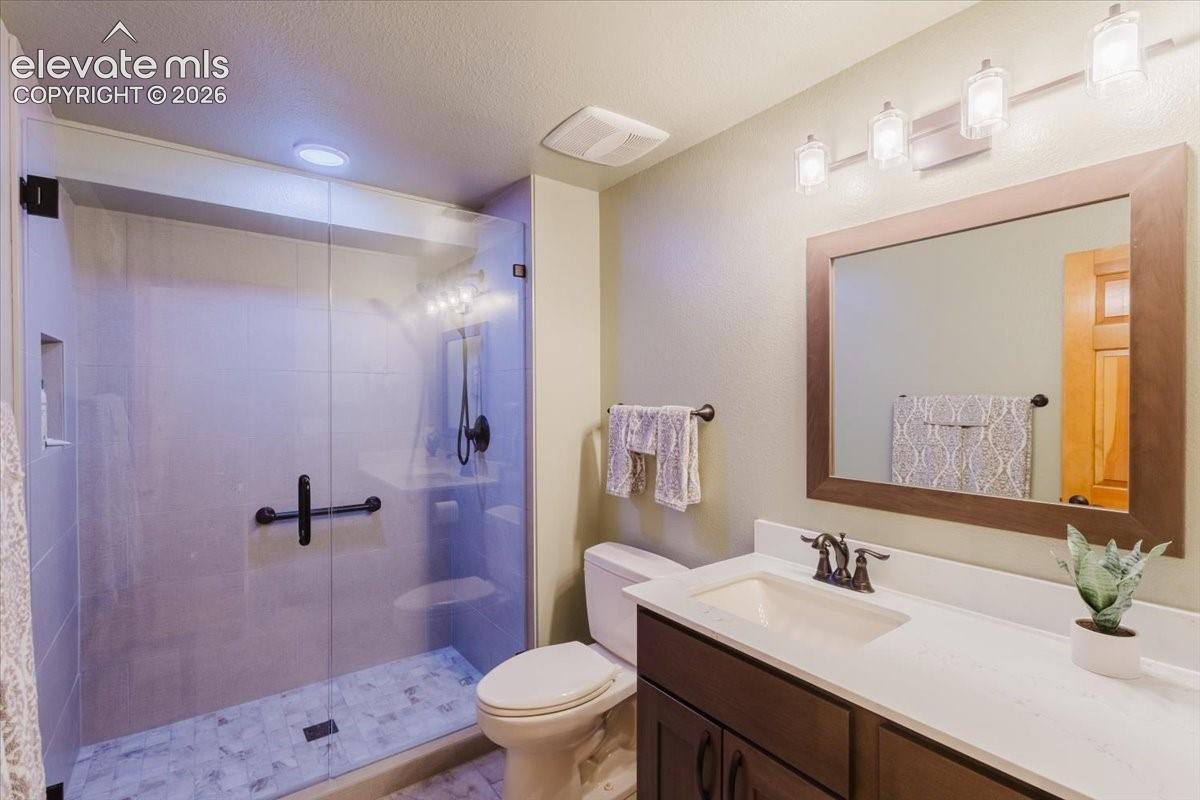Contemporary bathroom featuring a spacious glass-enclosed shower, a large vanity with a white countertop, a bronze-framed mirror, and a wall-mounted light fixture with four glass shades