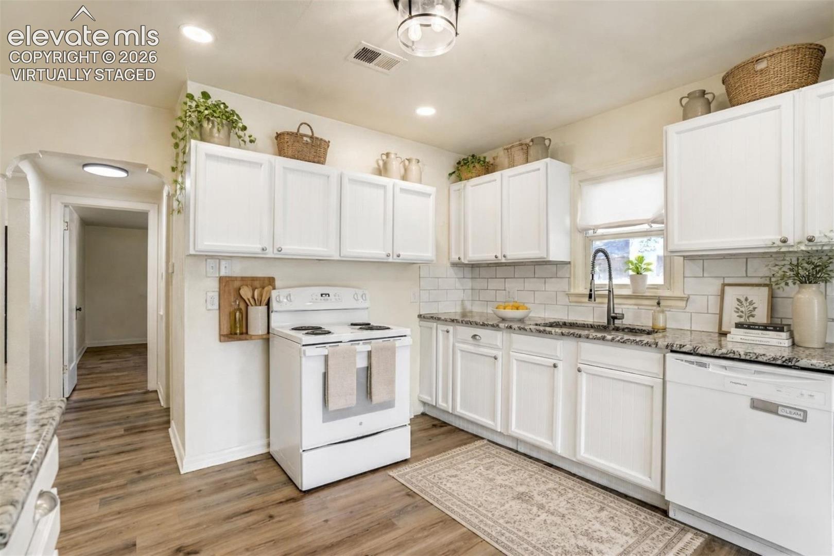 Virtually Staged.  Kitchen featuring white cabinetry, stone-finish countertops, subway tile backsplash, wood-finish flooring, and a single-basin sink with a gooseneck faucet
