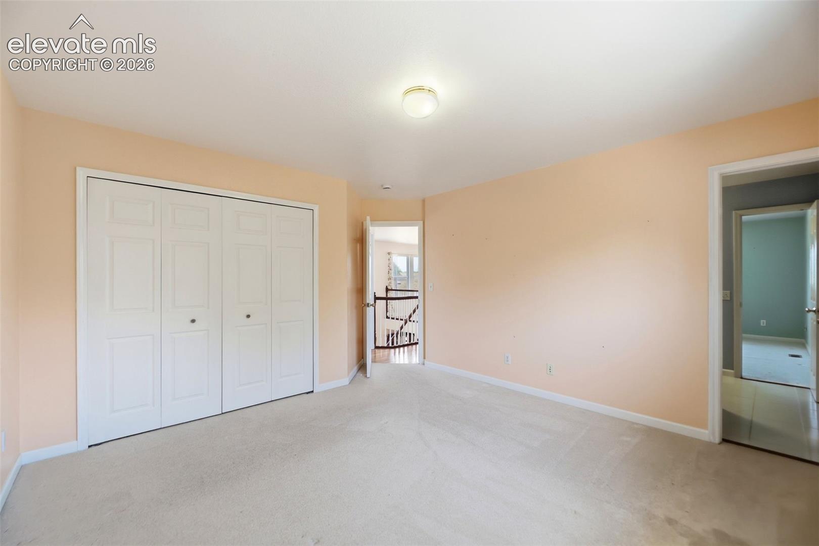 Spacious room featuring neutral carpeting, a large bi-fold door closet, and light-toned wall paint