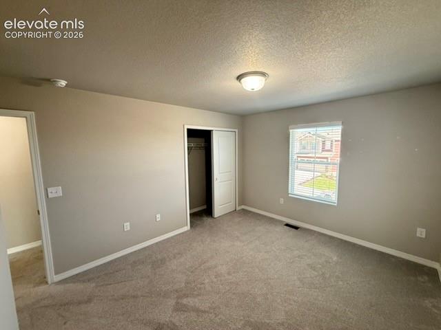 Neutral tone wall paint with a textured ceiling, carpeted flooring, window with blinds, and a built-in closet with bi-fold doors