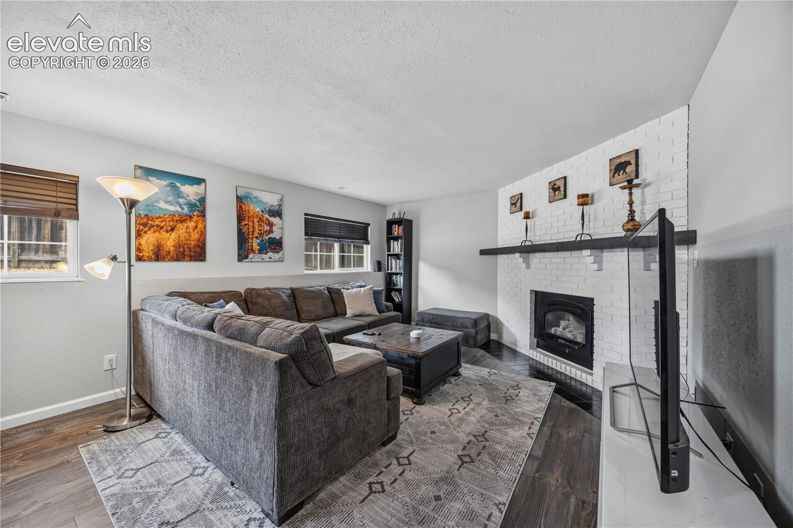 Painted white brick fireplace featuring a black mantel and wood-finish flooring