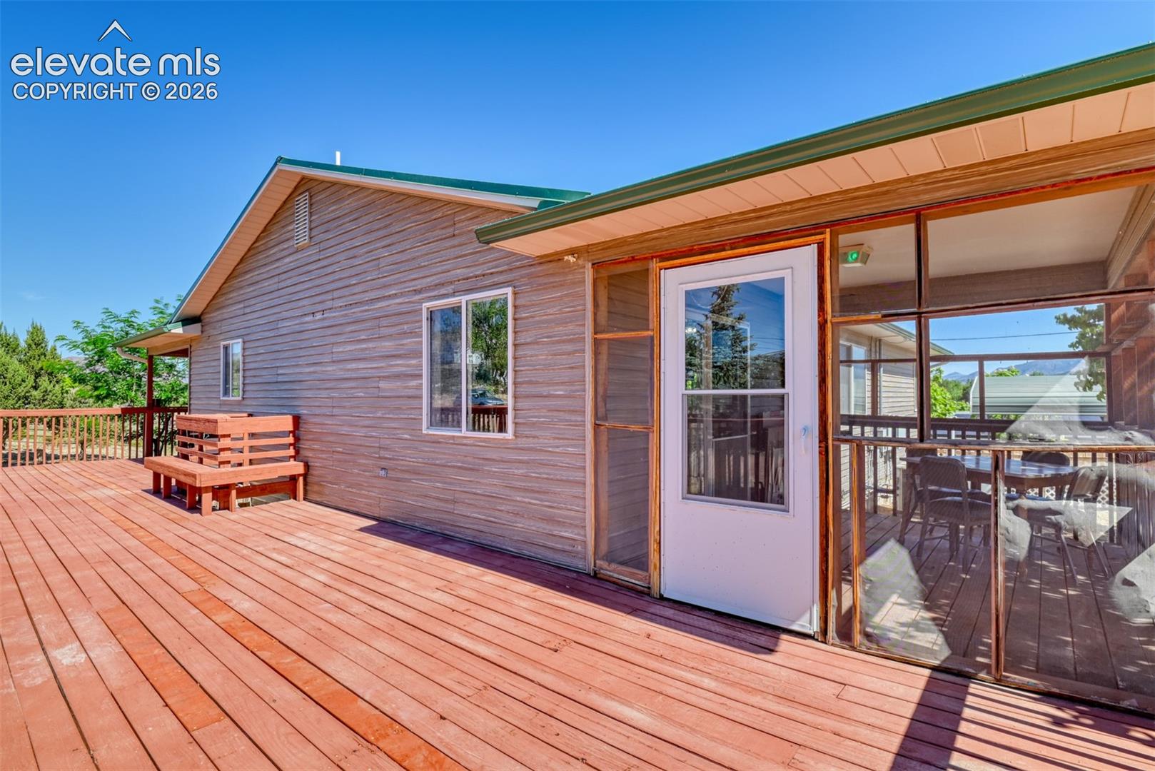 Exterior deck featuring wood-plank flooring, a built-in wooden bench, and a screened-in enclosure with a white door