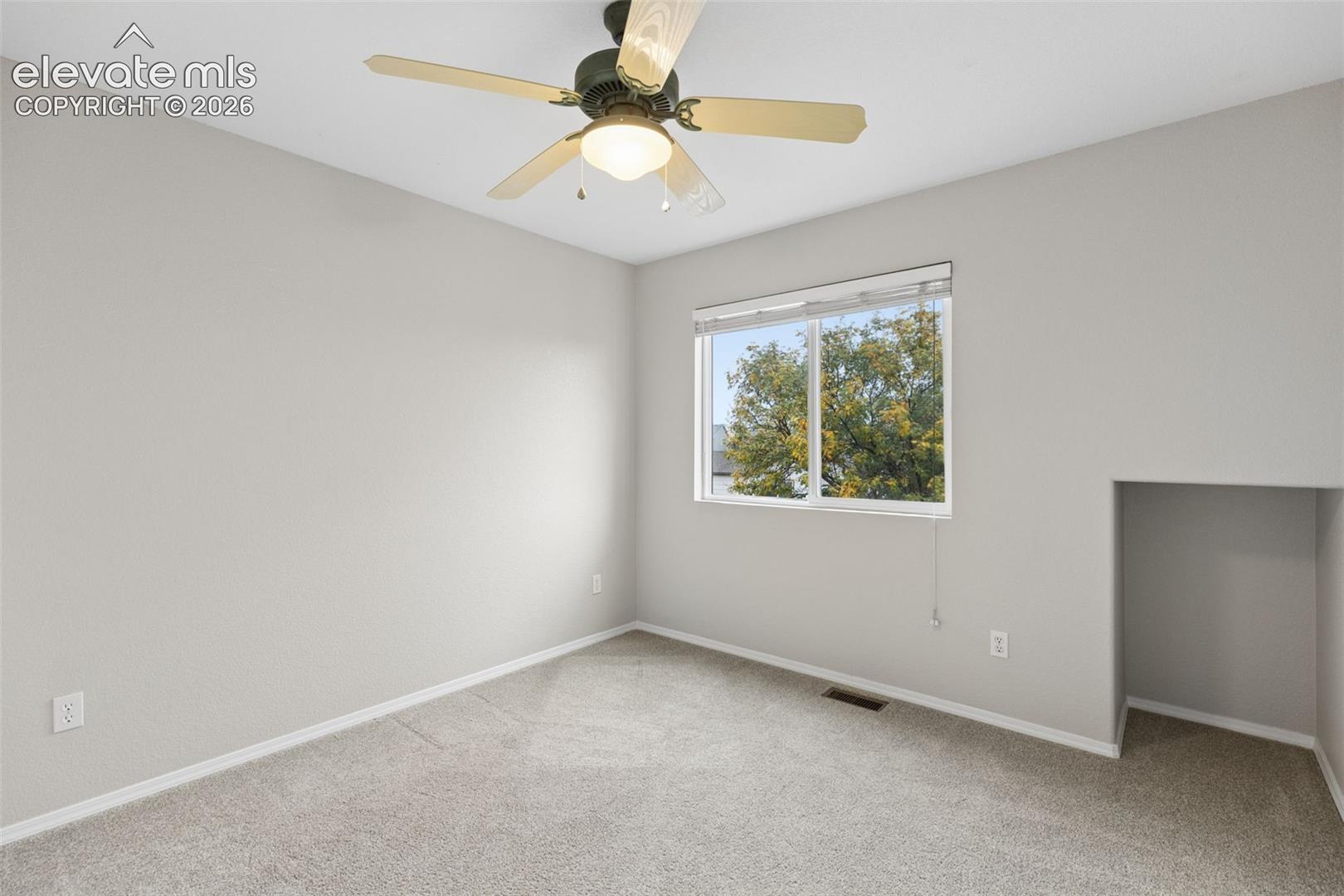 Neutral interior room featuring neutral-toned carpeting, a ceiling fan with integrated lighting, a sliding window with blinds, and an integrated wall alcove